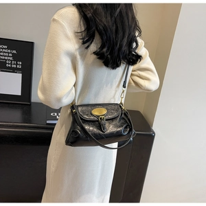 Detail of black vintage pleated shoulder bag with gold hardware on white dress