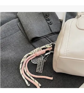 Detail view of woven ropes and metal tennis racket charms on a stylish white pillow bag