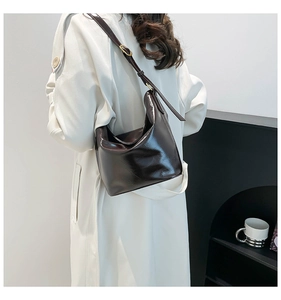 Detail view of glossy dark brown leather bucket bag with slim adjustable shoulder strap