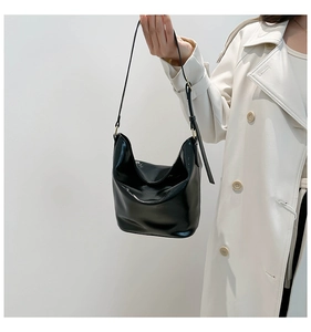 Detail of glossy black patent leather shoulder bag with adjustable strap on model