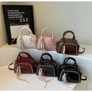 Macro detail of glossy boston bags showing contrast white stitching and fringe charms