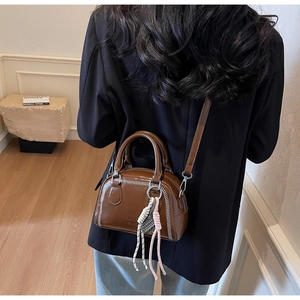Detail of a brown Boston bag with white stitching and stylish braided strap ornament