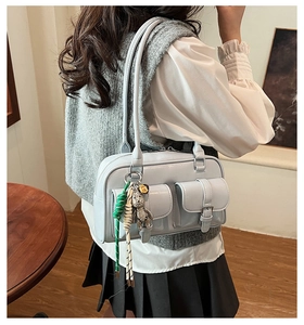 Detail of light blue glossy Boston bag with buckle pockets and a bear charm accessory