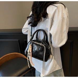 Detail of black patent leather pillow bag with white stitching and woven rope charm