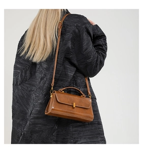 Detailansicht einer braunen Vintage-Lederhandtasche mit goldenem Schloss an einem Model