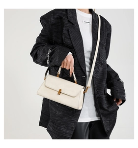 Detail einer minimalistischen beigen Umhängetasche mit goldener Schließe am Model