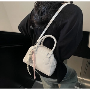 Detail view of a white mini Boston bag featuring woven rope pendants and crossbody strap