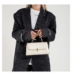Nahaufnahme der beigen Lederhandtasche mit Goldschließe auf schwarzem Blazer