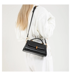 Schwarze glänzende Handtasche in Knitteroptik mit goldenem Verschluss am weißen Outfit