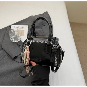 Detail of black PU leather bag featuring white contrast stitching and colorful woven charm