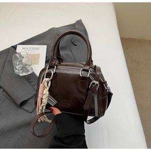 Close-up of brown patent leather pillow bag with baseball stitching and metal ring handle