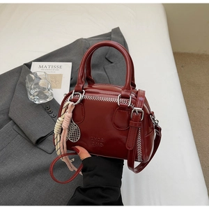 Detail of burgundy pillow bag with white baseball stitching and tennis racket charm