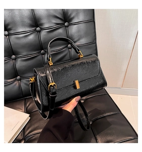 Detail der glänzenden schwarzen Handtasche mit Faltenstruktur und goldener Schnalle
