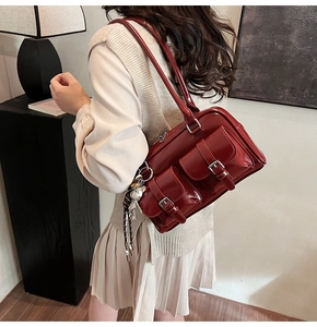 Detail of dark burgundy patent leather boston bag with outer pockets and teddy charm