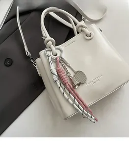 Detail of cream white bucket bag featuring a woven strap and metal badminton charms