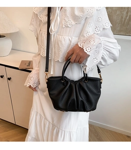 Détail d'un sac à main noir en cuir grainé avec ferrures dorées et bandoulière