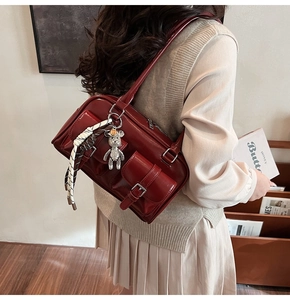 Dettaglio borsa Boston rosso scuro in pelle PU con tasche con fibbia e ciondolo a orsetto
