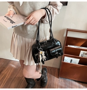 Detail of black glossy Boston shoulder bag with metallic buckles and bear charm