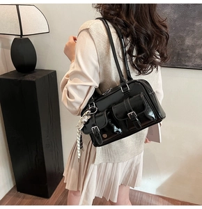 Detail of black glossy shoulder bag featuring double front pockets and animal charm