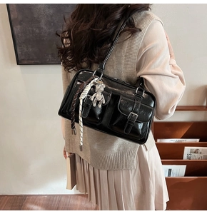 Detail view of glossy black shoulder bag with multi-pockets and rhinestone bear charm