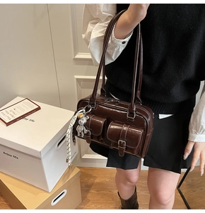 Detail of dark brown glossy patent leather shoulder bag with silver bear charm and front pockets