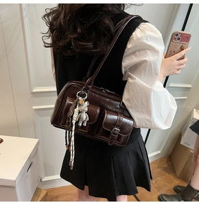 Detail of dark brown glossy leather Boston bag with pocket buckles and bear charm