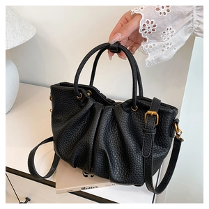 Détail de la texture grainée noire et des plis sur le sac à main avec finitions dorées