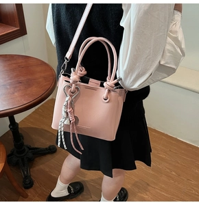 Pink oily leather bucket bag with heart charm and tassel detail worn by a model