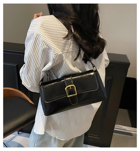 Détail du sac baguette noir brillant avec boucle dorée porté sur l'épaule