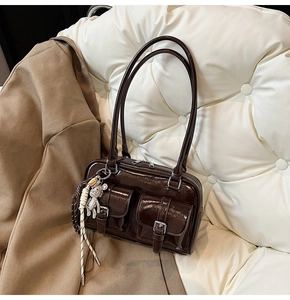 Detail of glossy brown underarm bag with silver buckles and a cute teddy bear charm