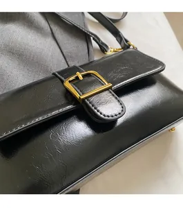 Détail d'un sac baguette noir brillant avec boucle dorée et rabat rectangulaire chic