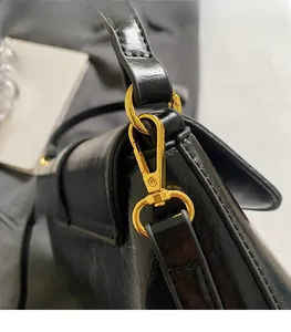 Vue macro d'un sac en cuir noir brillant montrant le crochet doré et les coutures fines