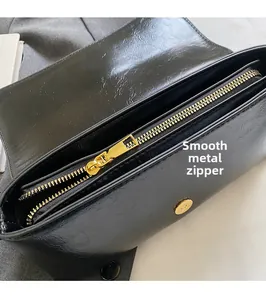 Détail d'un sac baguette en cuir ciré noir avec fermeture éclair dorée et boucle magnétique