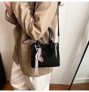 Detail of glossy black leather bucket bag with fashion charm and woven pendant decoration