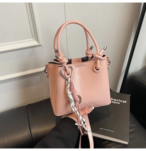 Detail of pink bucket bag with knotted handle and woven lanyard on leather surface