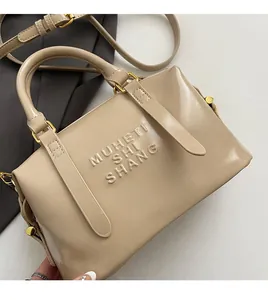 Detail of beige glossy leather handbag featuring embossed text and golden metal hardware