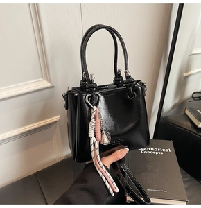 Detail of black glossy bucket bag with Fashion embossing and a braided tassel charm