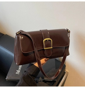 Détail du sac porté épaule marron foncé brillant avec boucle dorée sur un canapé