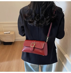 Détail du sac baguette en cuir mat bordeaux avec une boucle en métal doré et bandoulière