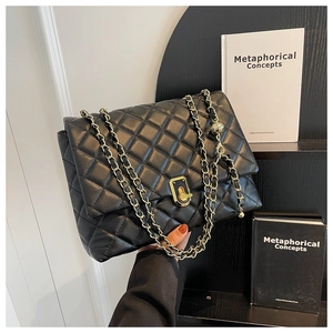 Close-up of black quilted leather shoulder bag with gold chain strap and square metal lock