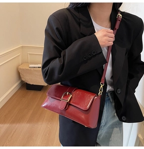 Détail du sac baguette rouge foncé brillant avec boucle dorée porté par le mannequin