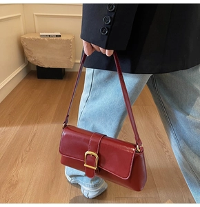 Détail d'un sac baguette en cuir verni rouge foncé avec boucle dorée porté à l'épaule