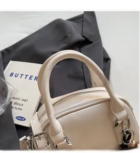 Detailed view of cream-colored bowling bag with silver hardware on a gray blazer