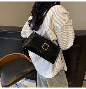 Détail du sac baguette noir brillant avec boucle dorée porté à l'épaule du mannequin