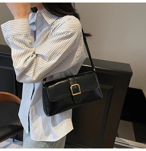 Détail d'un sac baguette en cuir noir brillant avec une boucle dorée sur un mannequin