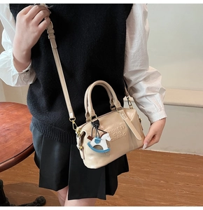 Detail of beige boston bag with letter embossing and cute rocking horse charm