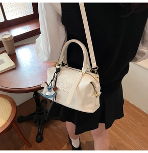 Detail of cream white Boston bag with embossed lettering and blue pony charm in a cafe