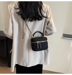 Detail of black tweed crossbody bag with gold chain strap on a beige blazer background