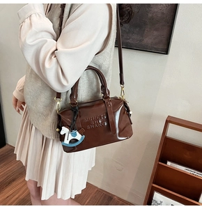 Detail of dark brown retro Boston bag with embossed logo and horse charm attachment