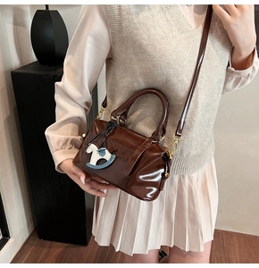 Close-up of dark brown patent leather boston bag with embossed logo and pony charm